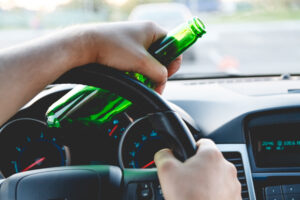 Person’s hand on steering wheel of car holding an alcohol bottle, drunk driving accident